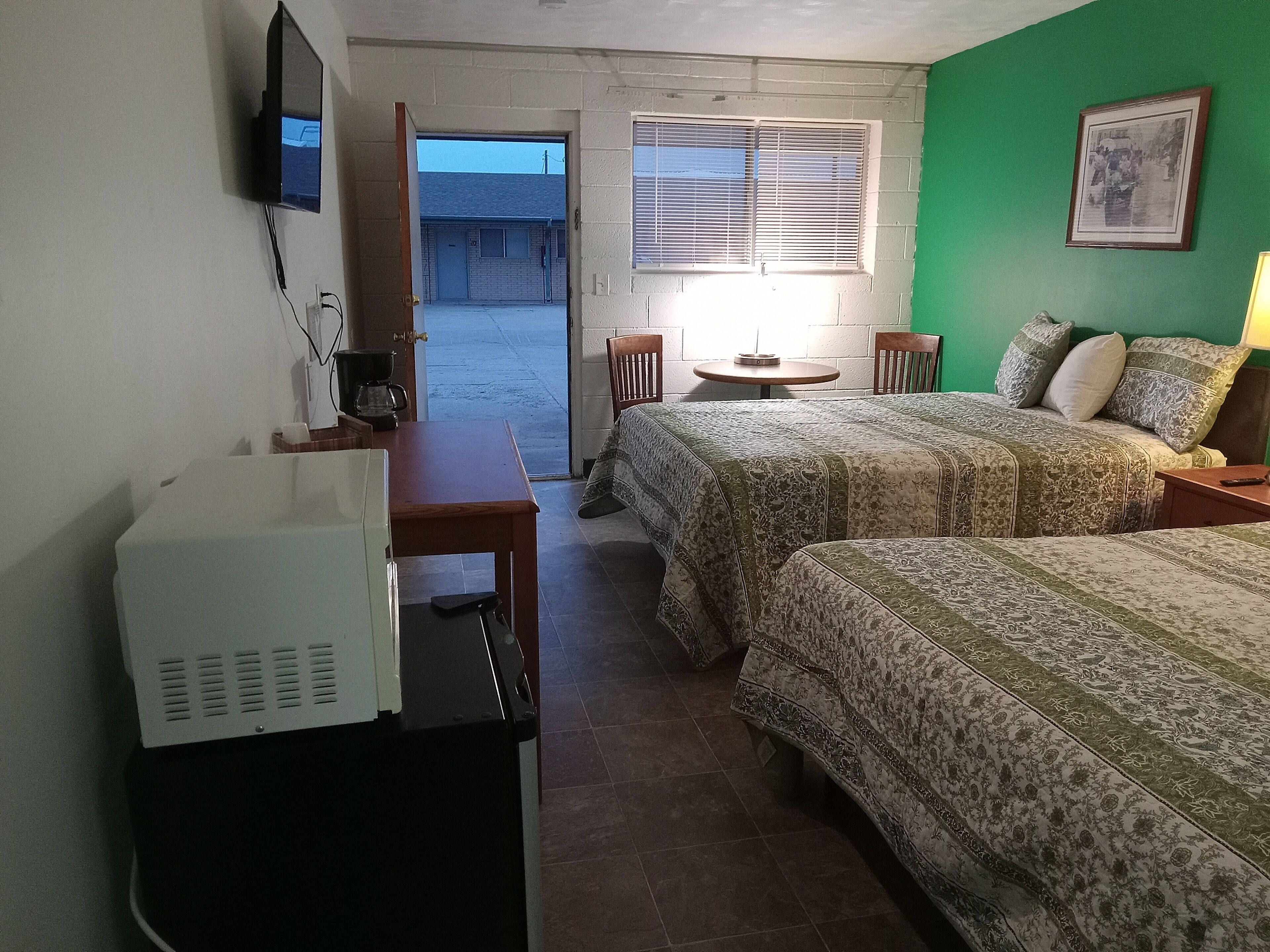 Una habitación de hotel con dos camas, un escritorio, una silla, un televisor y una ventana con persianas.