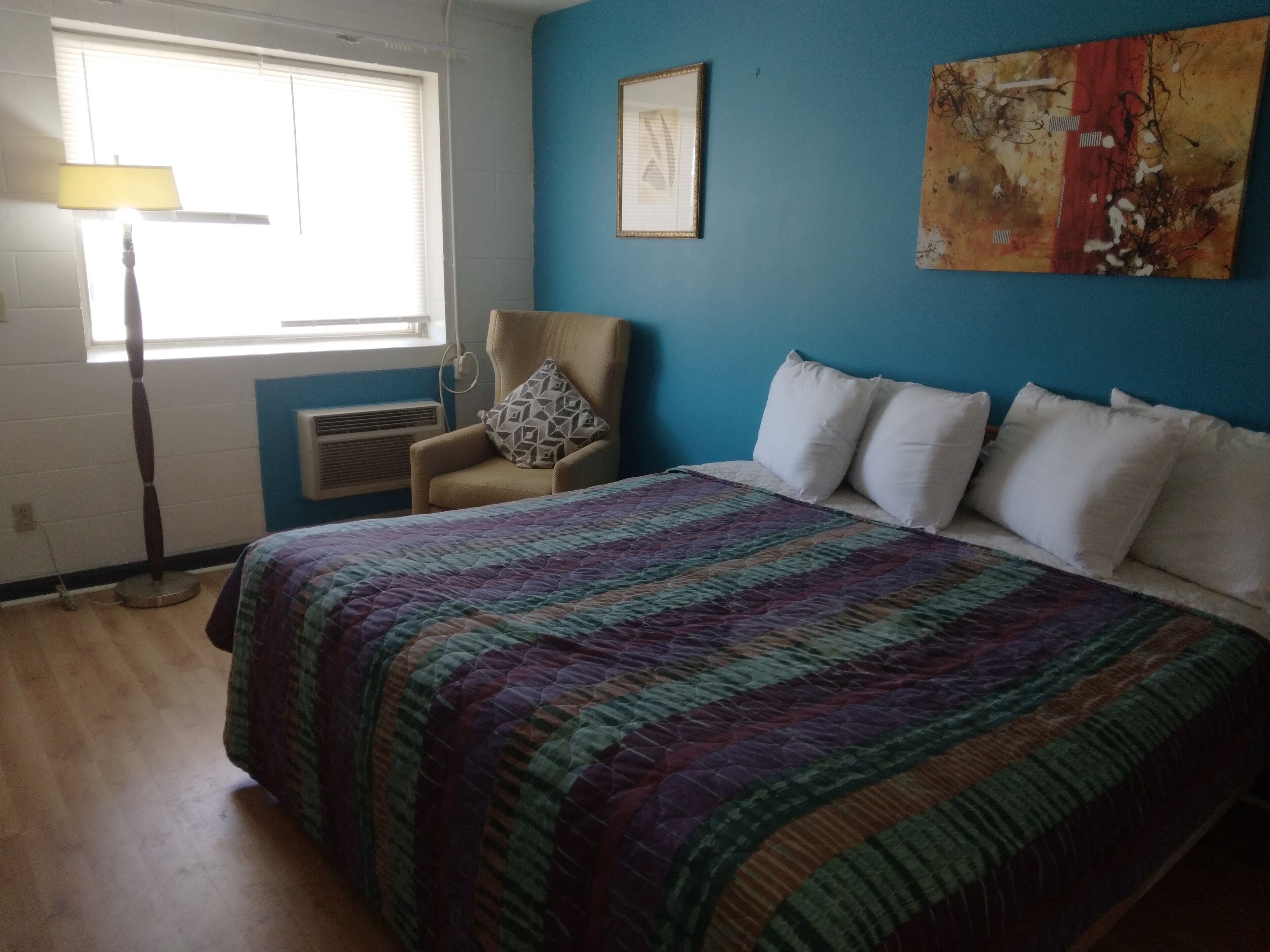 Een slaapkamer met een bed, een stoel, een raam en een schilderij aan de muur.