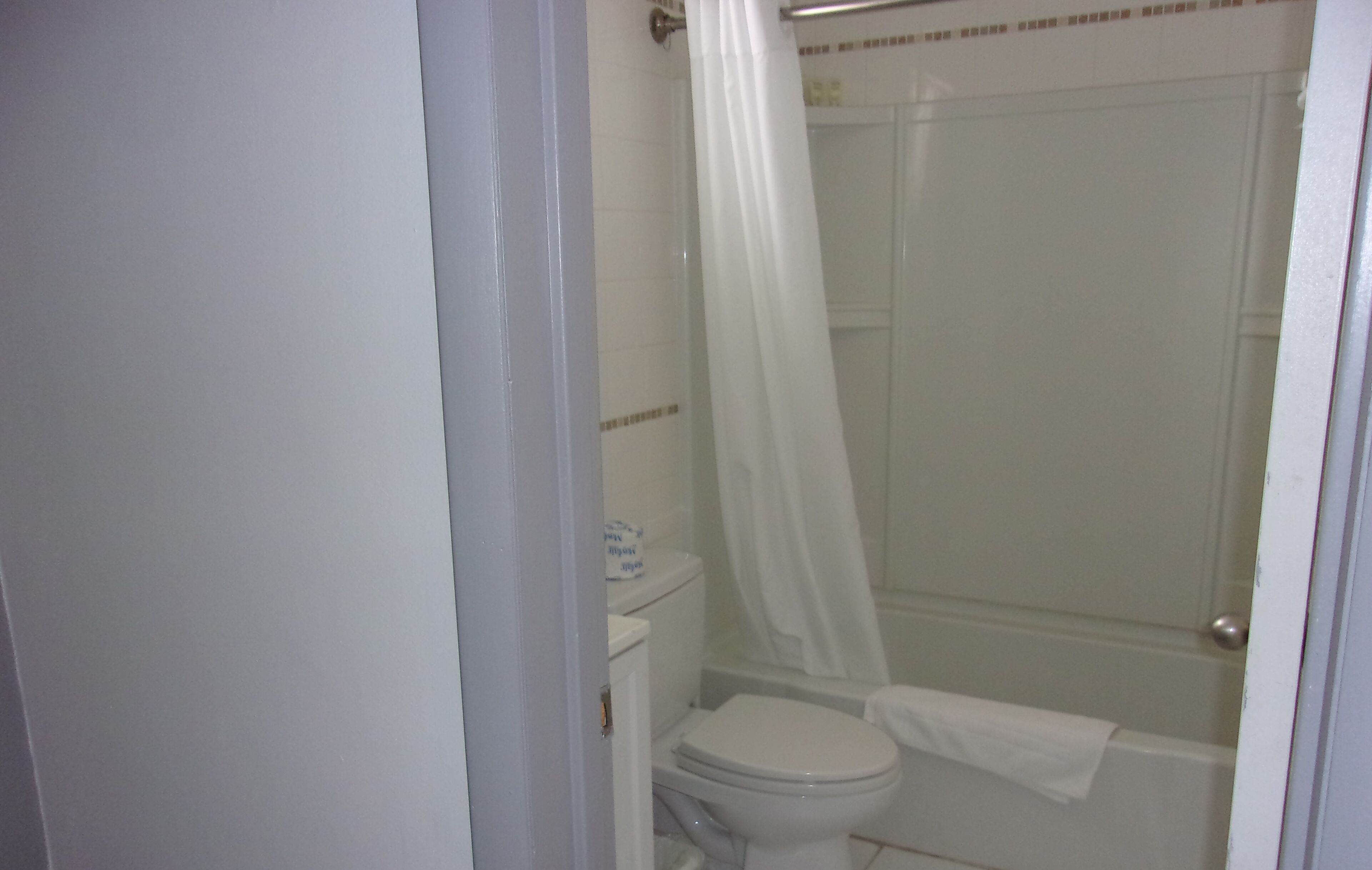 Un baño con inodoro, ducha con cortina y una toalla colgada en la pared.