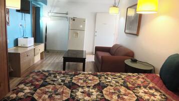 A room with a bed, a desk, a chair, a small table, a lamp, and a door.