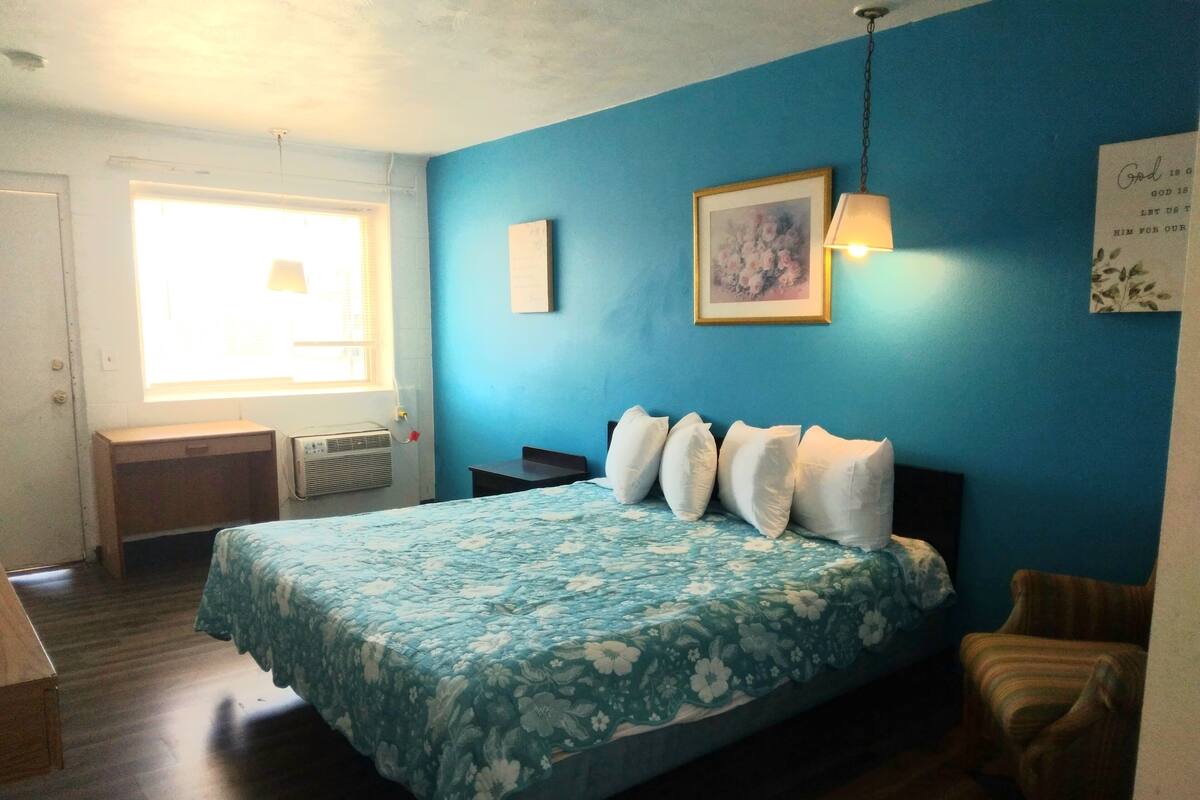 Une chambre à coucher avec une couvre-lit à motifs floraux, une fenêtre avec des stores, un bureau et une chaise.