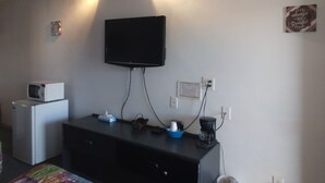 A room with a flat-screen TV mounted on the wall, a microwave, a coffee maker, and a dresser with various items on top. - Capri Motel (Scottsbluff)