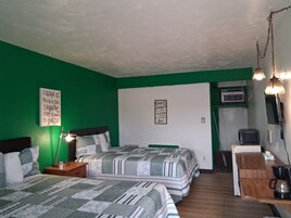 Una habitación con dos camas, un escritorio con cafetera, una lámpara y carteles motivacionales en las paredes.