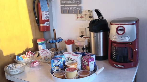 A kitchen counter with various breakfast items, a coffee maker, and a fire extinguisher. - Capri Motel (Scottsbluff)