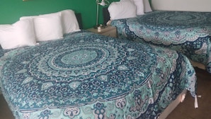 A hotel room with two beds, each with a patterned bedspread and white pillows. There is a nightstand with a lamp between the beds. - Capri Motel (Scottsbluff)