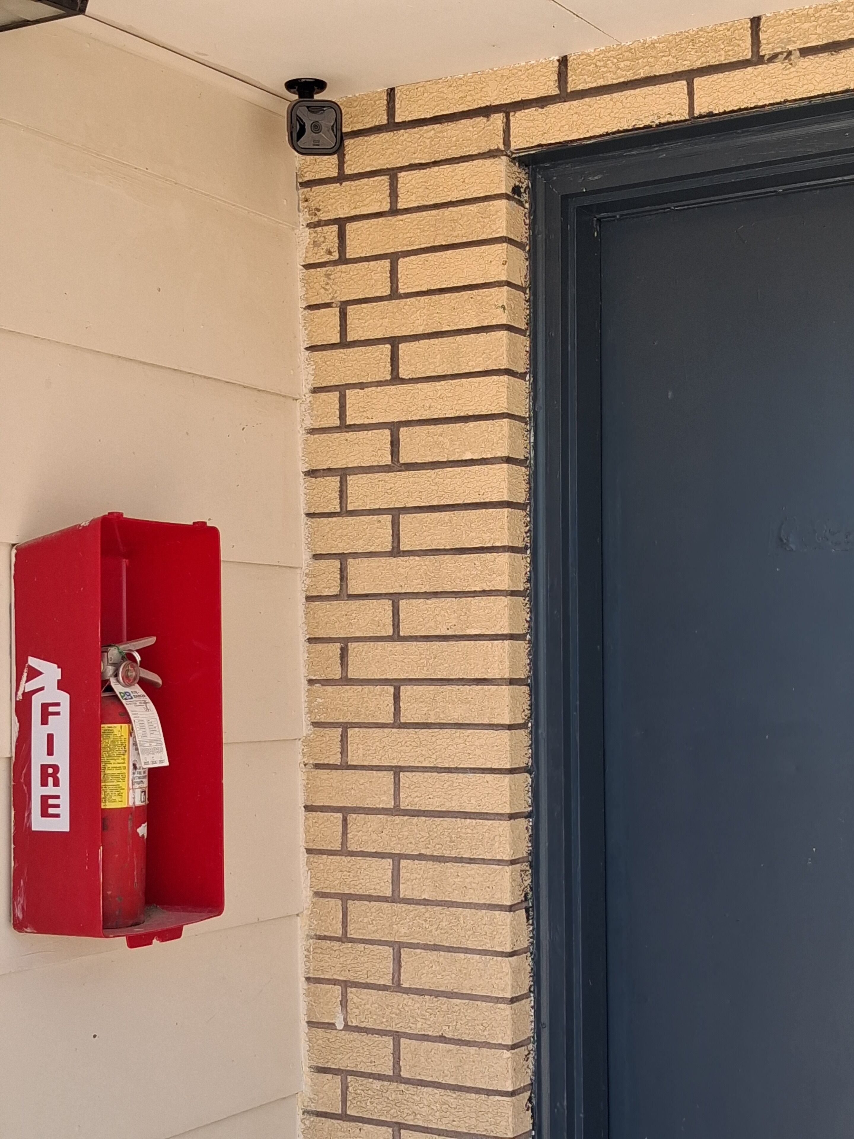 A red fire alarm box mounted on a beige wall next to a dark door.