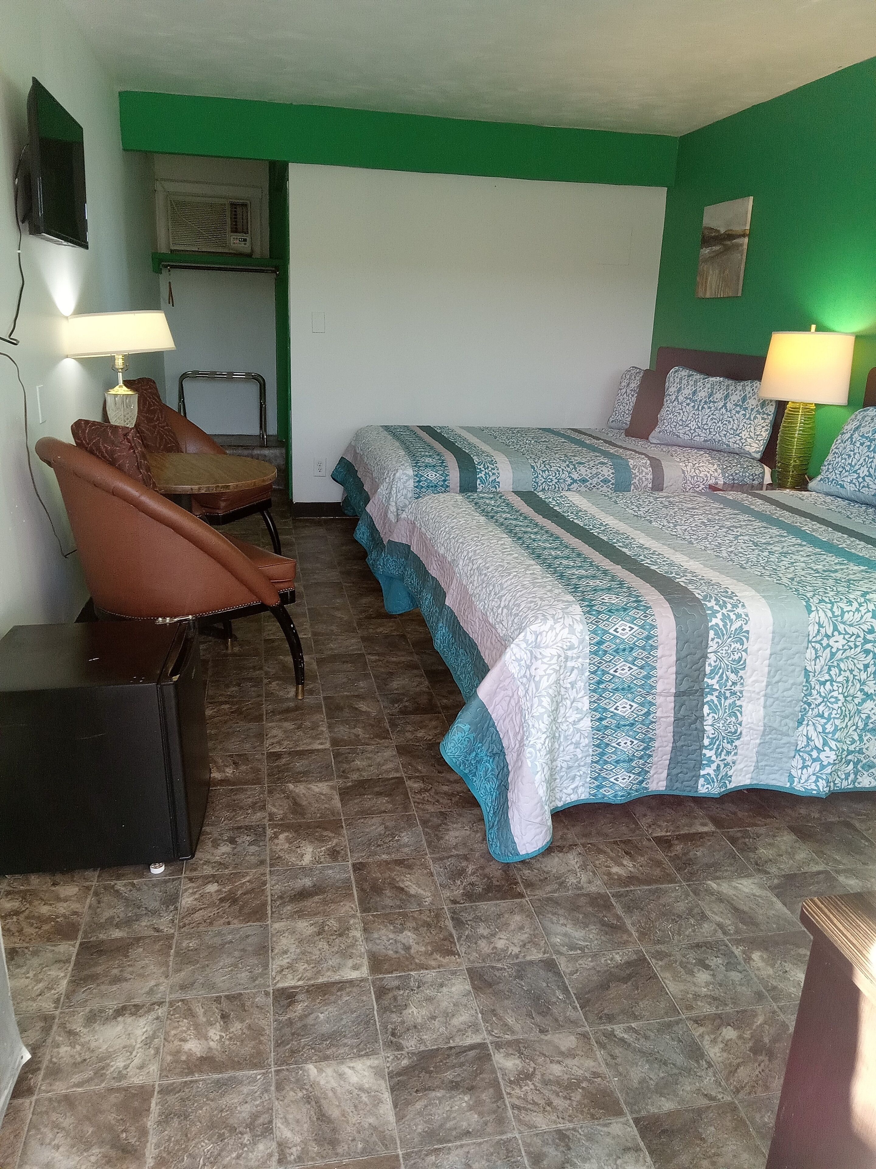 A room with two beds, a chair, a desk, and a TV.