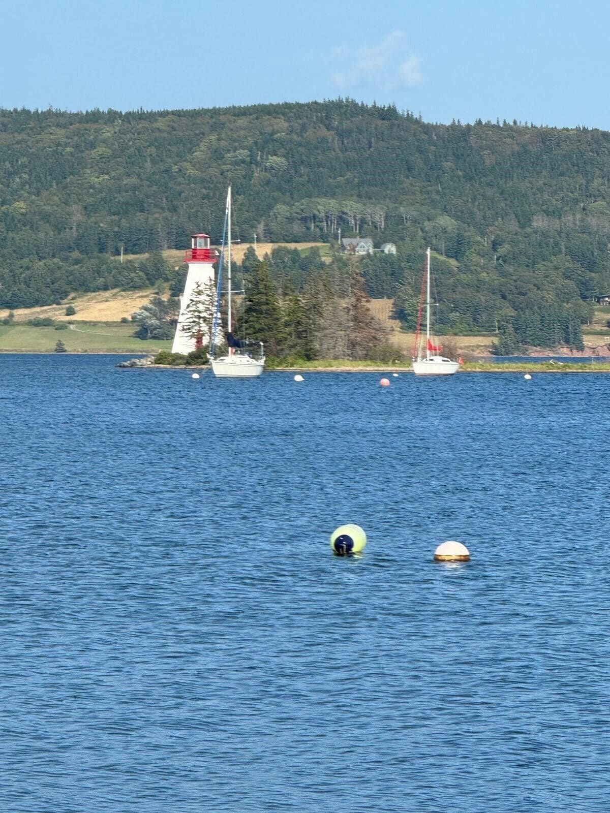 A lighthouse with a red top, surrounded by calm water and boats.