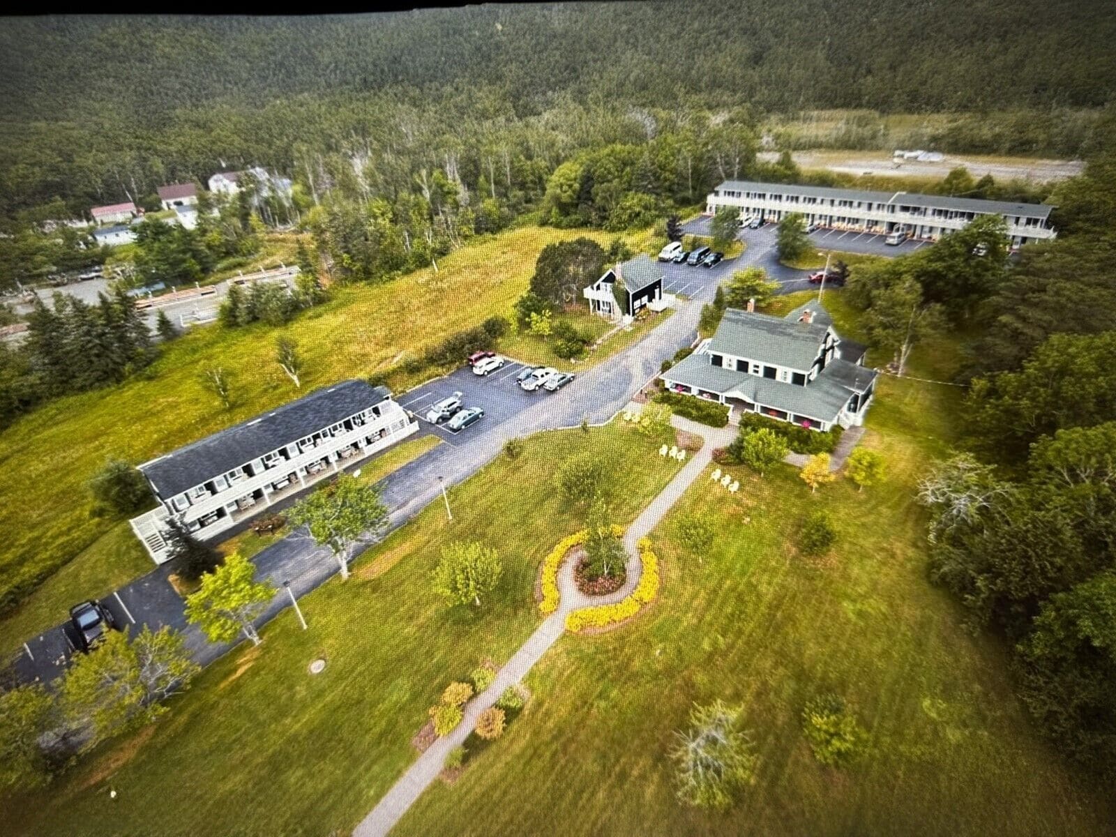 An aerial view of a hotel with multiple buildings, parking areas, and surrounding greenery.
