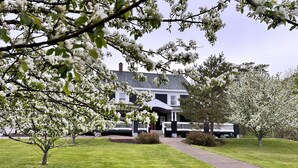 A two-story house with a white porch and a driveway leading to the entrance. - Ceilidh Country Lodge (Baddeck)