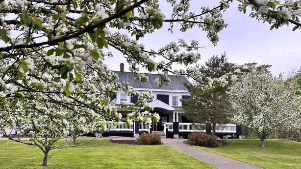 A two-story house with a white porch and a driveway leading to the entrance. - Ceilidh Country Lodge (Baddeck)