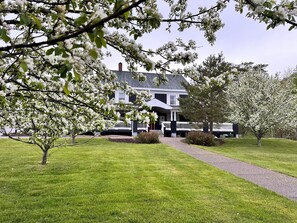 A two-story house with a white porch and a driveway leading to the entrance. - Ceilidh Country Lodge (Baddeck)