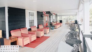 A covered porch with rows of wicker chairs and tables, a red rug, and a view of the outdoors. - Ceilidh Country Lodge (Baddeck)