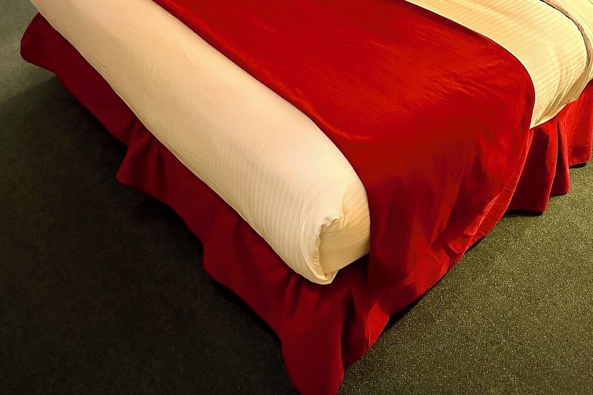 A neatly made bed with a red and white bedspread, a wooden headboard, and a bedside table with a lamp.