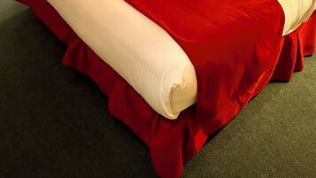A neatly made bed with a red and white bedspread, a wooden headboard, and a bedside table with a lamp.