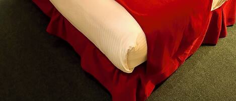 Una cama bien hecha con una colcha roja y blanca, un cabecero de madera y una mesita de noche con una lámpara.