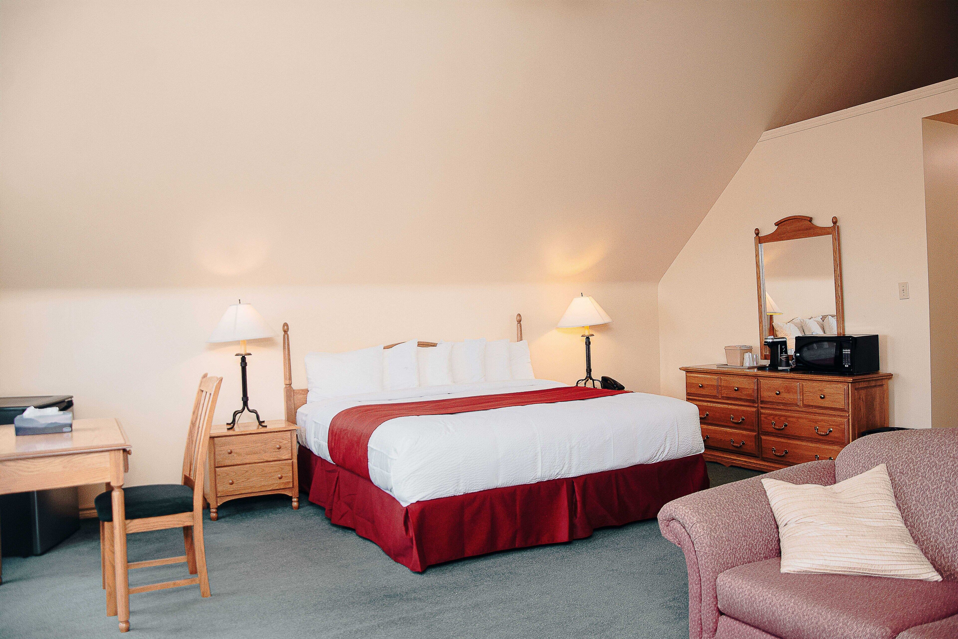 A hotel room with a bed, a desk, a chair, a dresser, and a couch.
