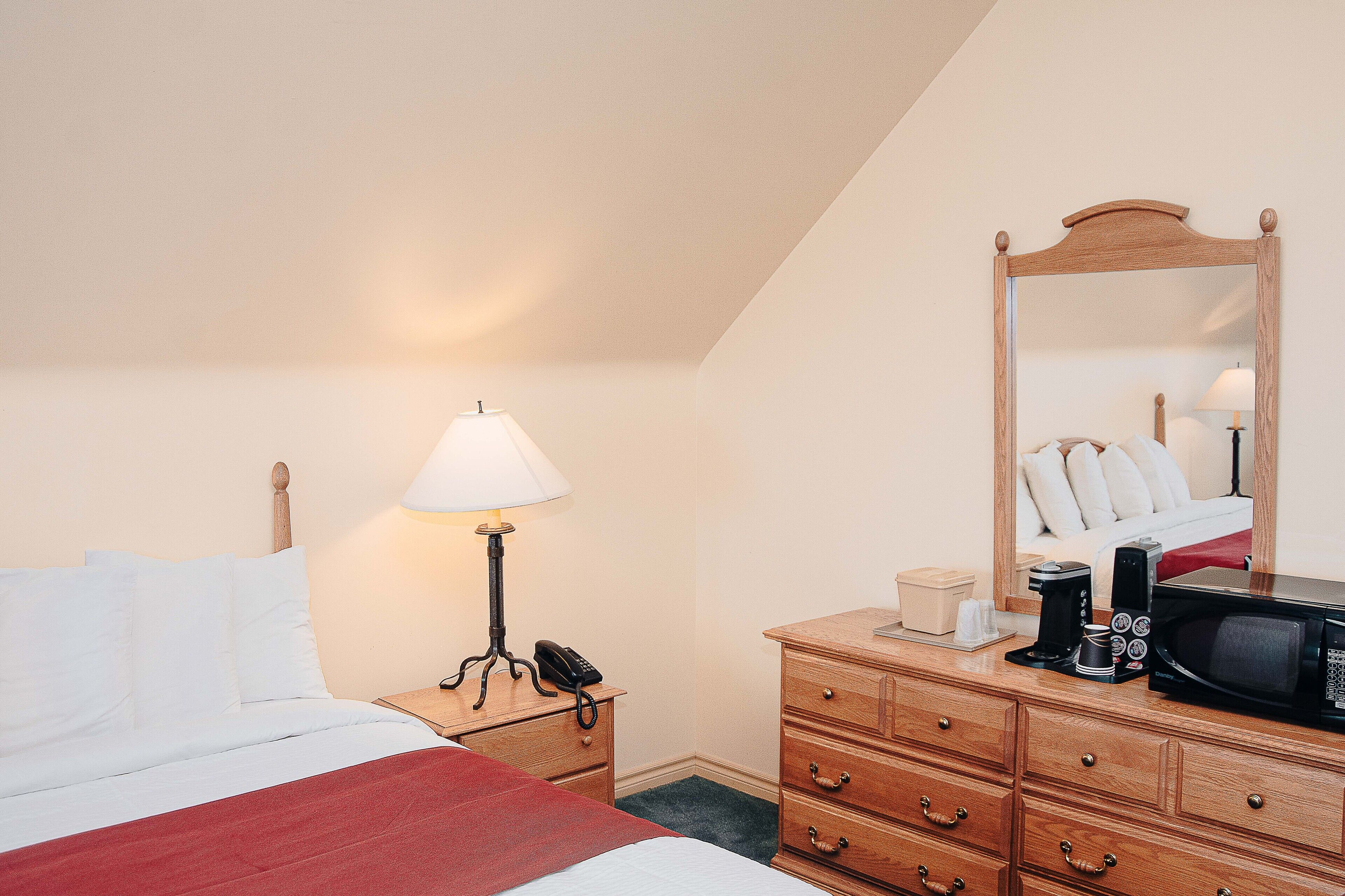 A hotel room with a bed, a bedside lamp, a wooden dresser, a mirror, and a microwave.