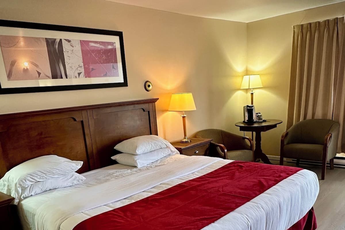 A hotel room with a large bed, two bedside tables, a chair, a desk, and a lamp.