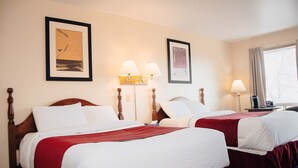 A hotel room with two beds, each with a red bedspread, white linens, and a wooden headboard. There are two wall-mounted lamps, a framed artwork above the left bed, and a window with curtains on the right. - Ceilidh Country Lodge (Baddeck)