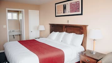 Een hotelkamer met een bed, twee nachtkastjes met lampen, een houten hoofdbord, een lijst met kunstwerk aan de muur, en een badkamer met spiegel en wastafel.