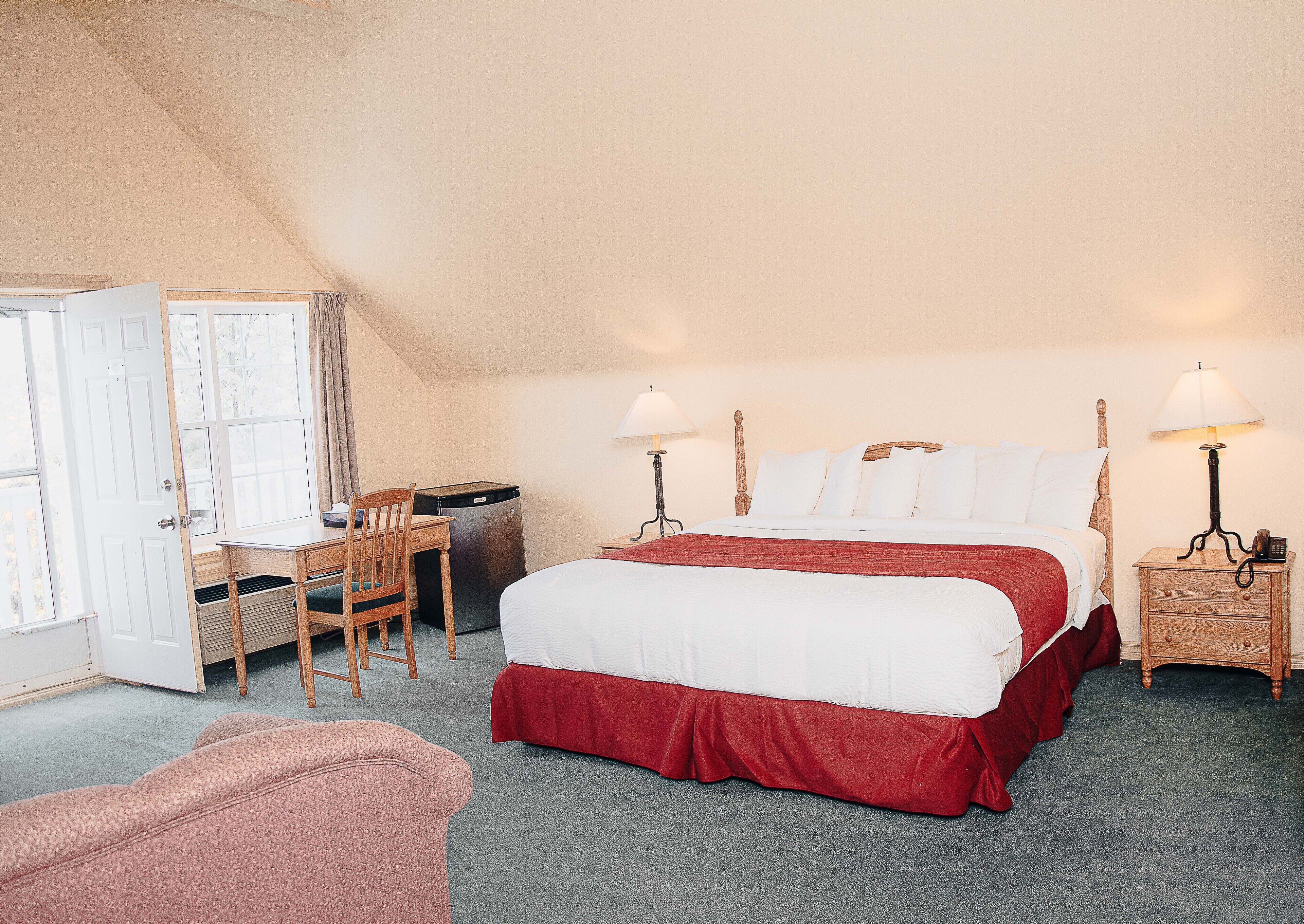 Ein Schlafzimmer mit Bett, Schreibtisch, Stuhl und kleinem Kühlschrank.