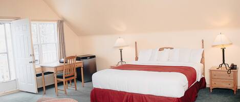 A bedroom with a bed, desk, chair, and a small refrigerator.