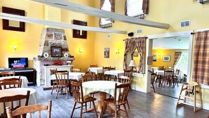 A restaurant with wooden tables and chairs, a stone fireplace, and yellow walls. - Ceilidh Country Lodge (Baddeck)
