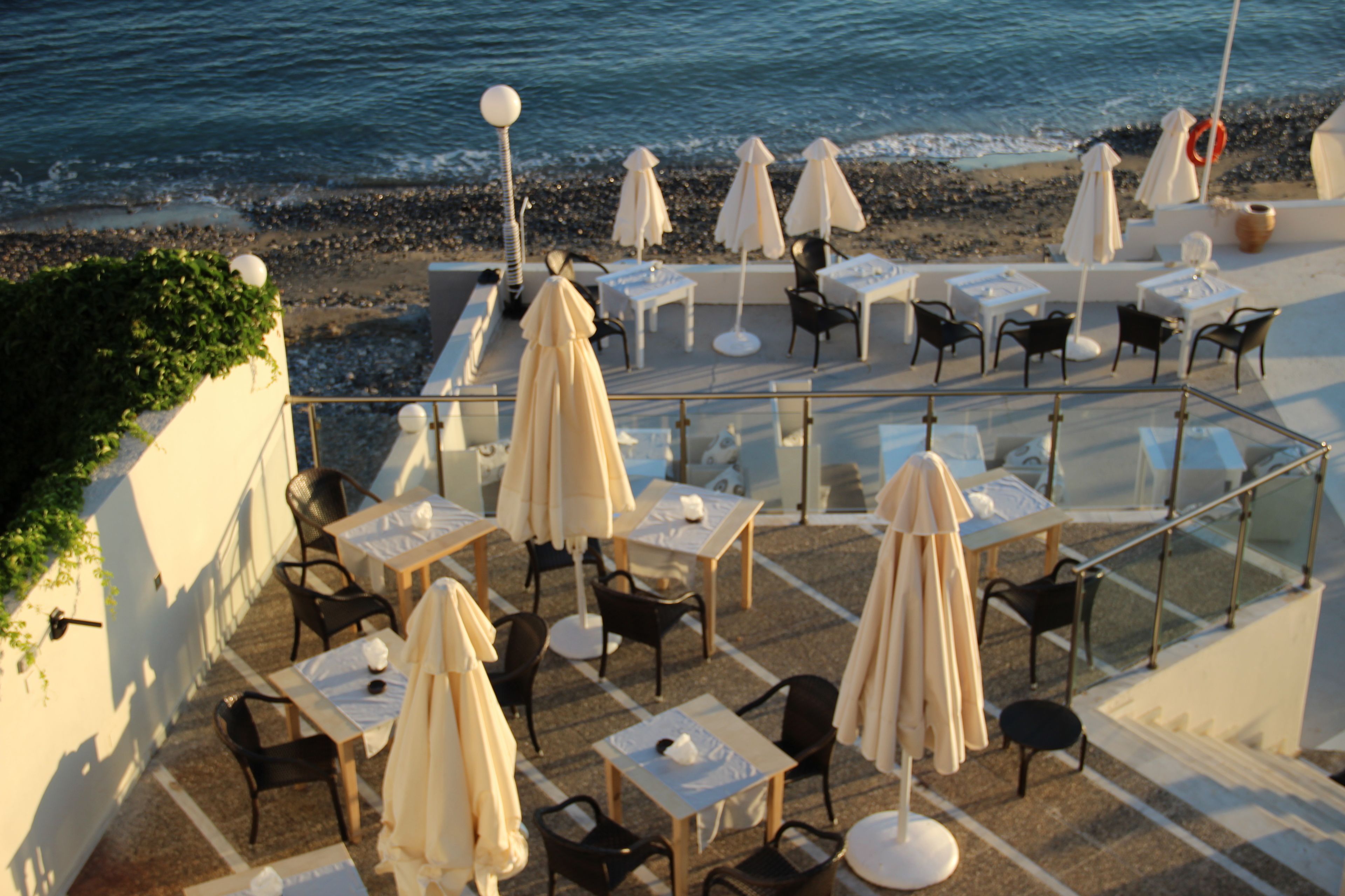 Una terraza exterior con mesas y sillas, sombrillas y vista al mar.