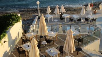 Una terraza exterior con mesas y sillas, sombrillas y vista al mar.