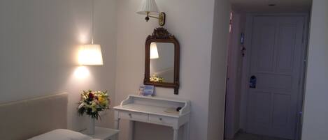 Una habitación de hotel con una cama, una mesita de noche con lámpara, un espejo y una puerta que da a otra habitación.