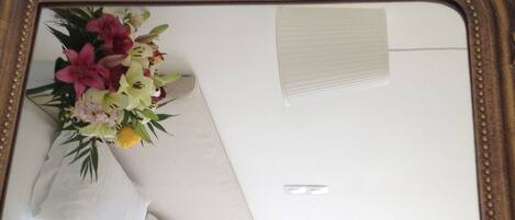 A mirror with a decorative frame reflecting a bouquet of flowers and a white pillow.
