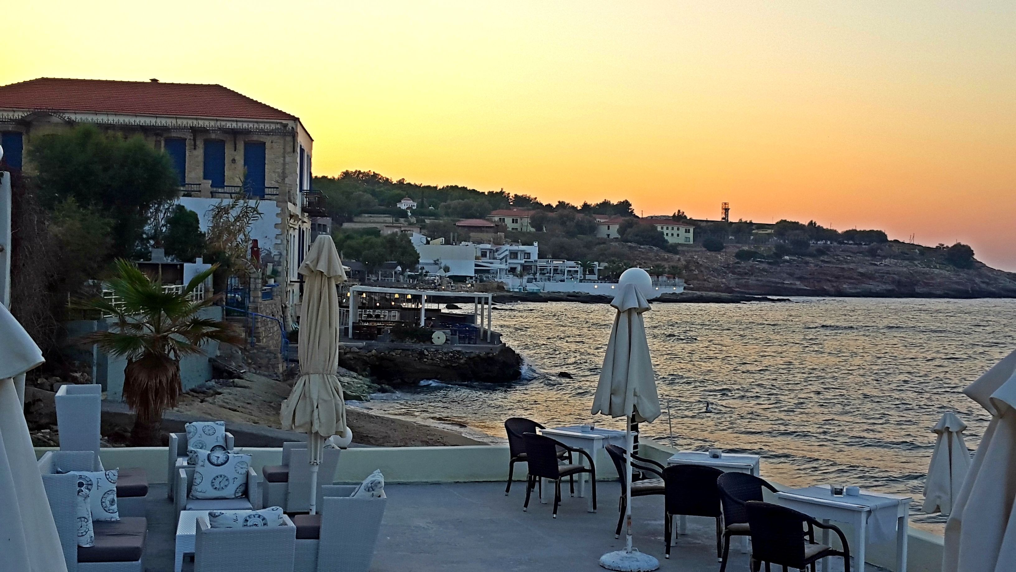 Eine Seeterrasse mit Außenplätzen und Blick auf das Meer, im Hintergrund sind Gebäude zu sehen.