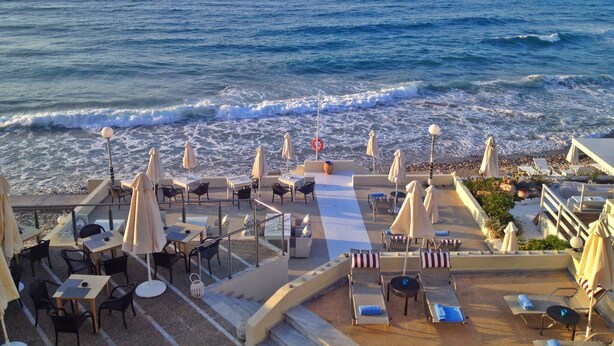 Une terrasse en bord de mer, avec des tables et des chaises, une bouée de sauvetage et une vue sur l’océan.