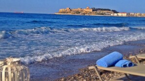 Une plage offrant une vue dégagée sur la mer, une structure imposante qui ressemble à un château au loin, et une chaise longue avec une serviette.