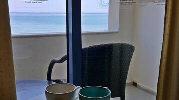 A balcony with a view of the sea, a table with a book and two bowls, and a chair.