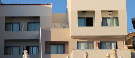 Un hotel moderno con varios balcones, mobiliario exterior con sombrillas y un cielo azul despejado.