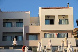 A modern hotel with multiple balconies, outdoor seating with umbrellas, and a clear blue sky. - Filoxenia Beach (Rethymno)