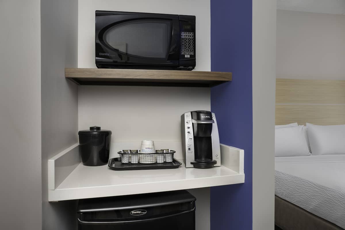 Habitación de hotel con un microondas en un estante, una cafetera y un cubo de basura.