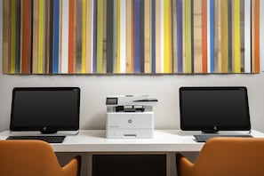 Two HP desktop computers on a white desk with an HP printer between them, and a colorful striped wall art above.