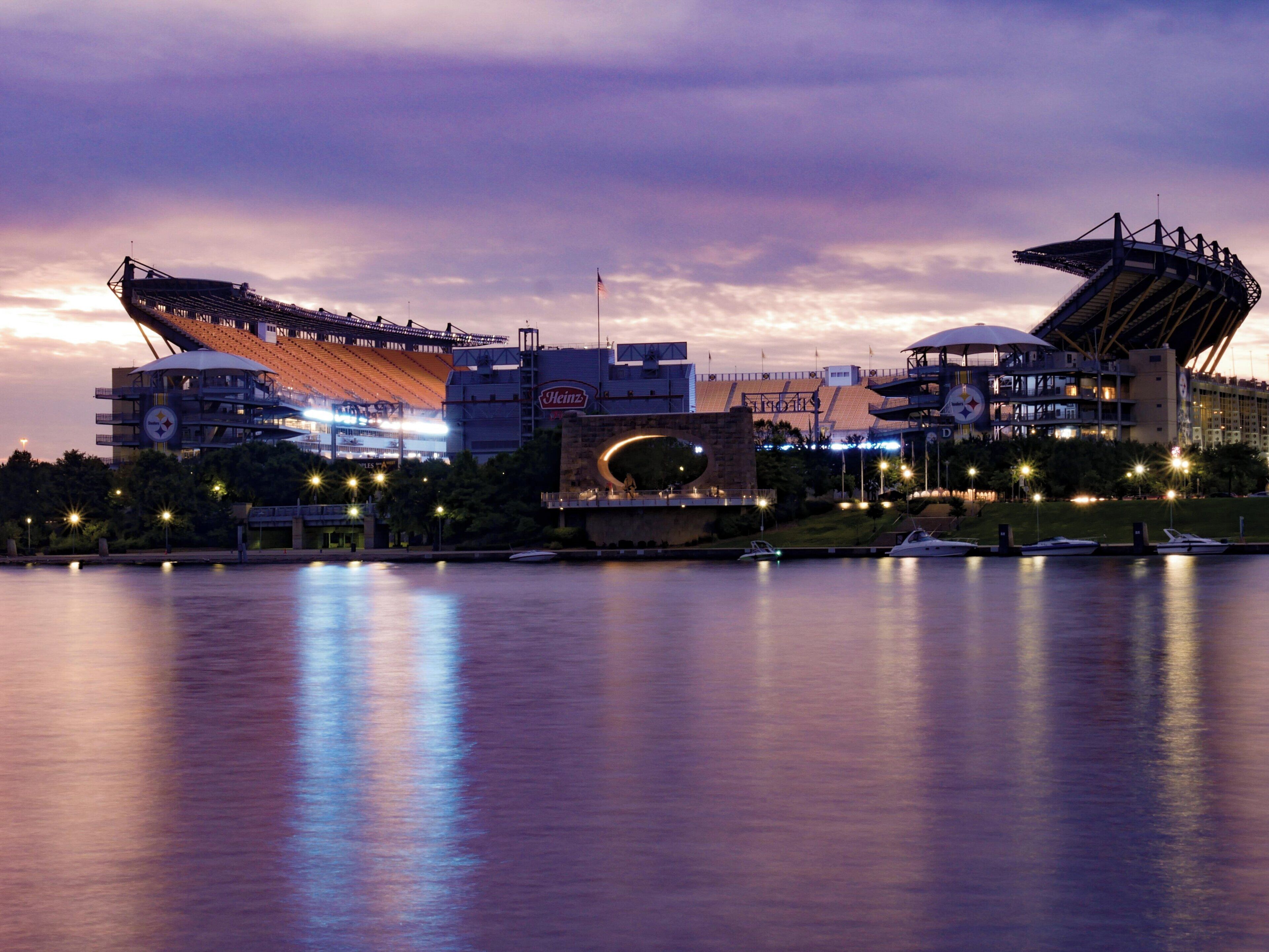 Um estádio com um grande letreiro Heinz, uma ponte e barcos na água.