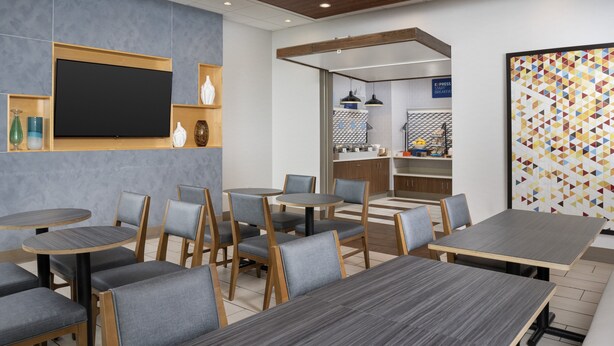 A modern cafe with round tables and chairs, a flat-screen TV, and a colorful geometric wall art piece.