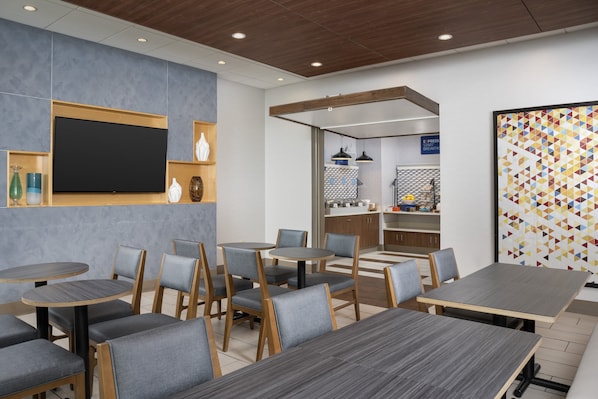 A modern cafe with round tables and chairs, a flat-screen TV, and a colorful geometric wall art piece.
