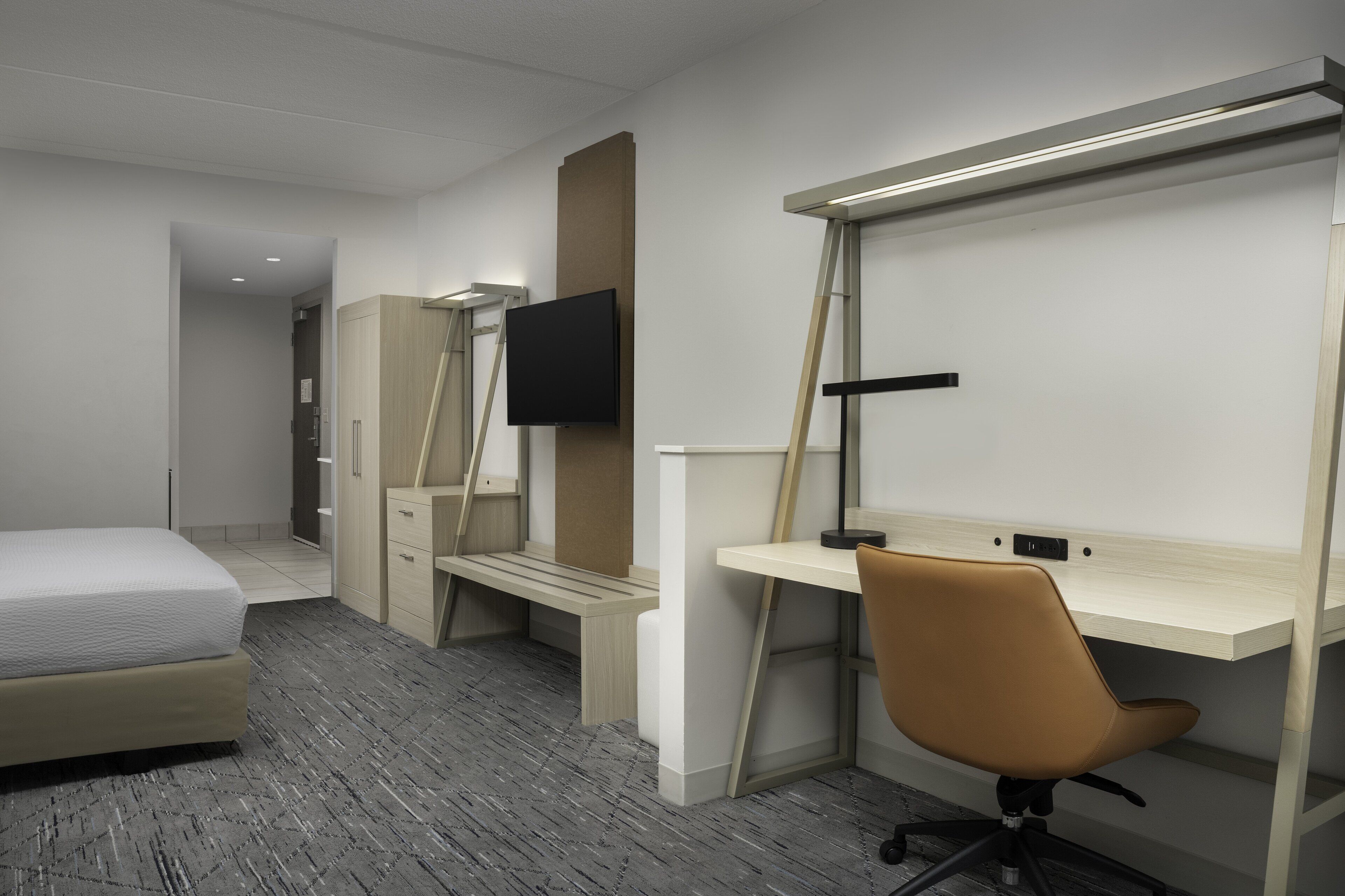 Une chambre d’hôtel comprenant un lit, un bureau avec une chaise, un téléviseur fixé au mur et une armoire.