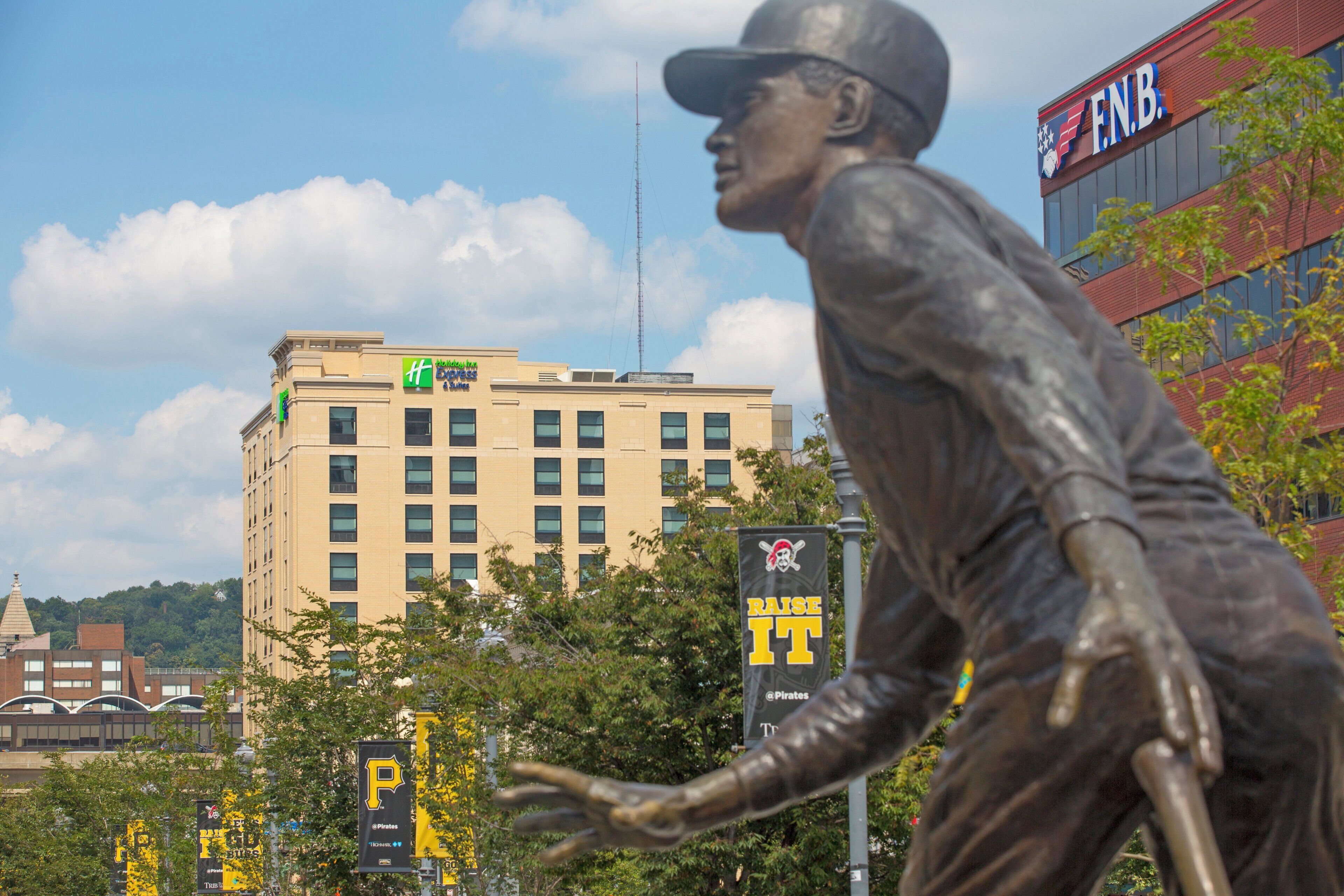 A statue of a baseball player in a stadium with a hotel and a building with a sign in the background.