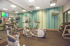 Ein Fitnessraum mit Laufbändern, Crosstrainern und einem Gewichtständer.