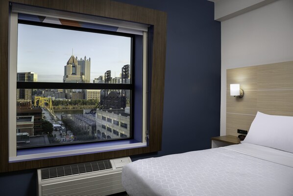 A hotel room with a large window, a bed, a bedside table, and a wall-mounted light fixture. - Holiday Inn Express & Suites Pittsburgh North Shore by IHG (Pittsburgh)