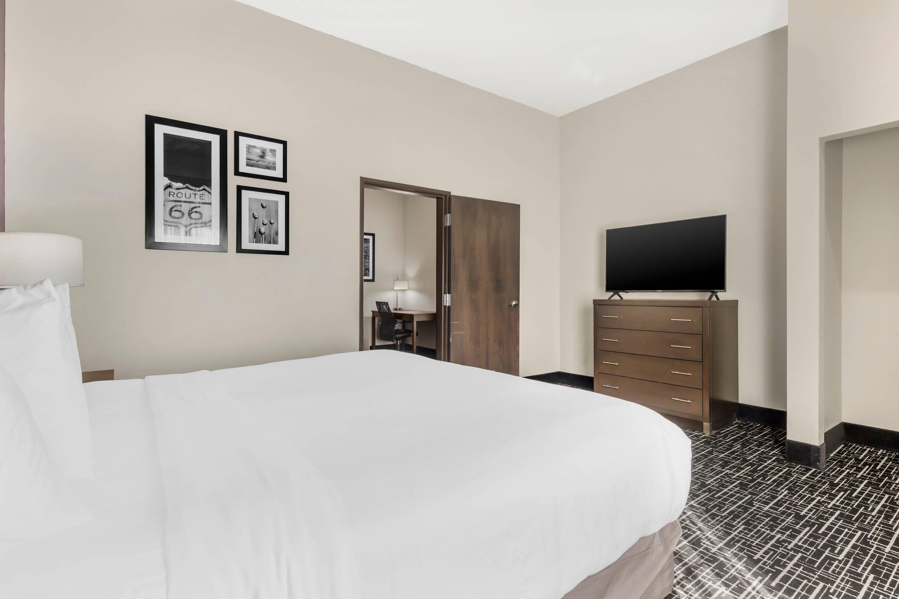 Une chambre d’hôtel avec un grand lit, un téléviseur à écran plat, une commode et des tableaux encadrés au mur.