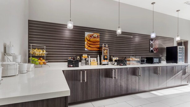 A modern kitchen with a long counter, stainless steel appliances, and a large waffle display. - Comfort Inn & Suites (Claremore)