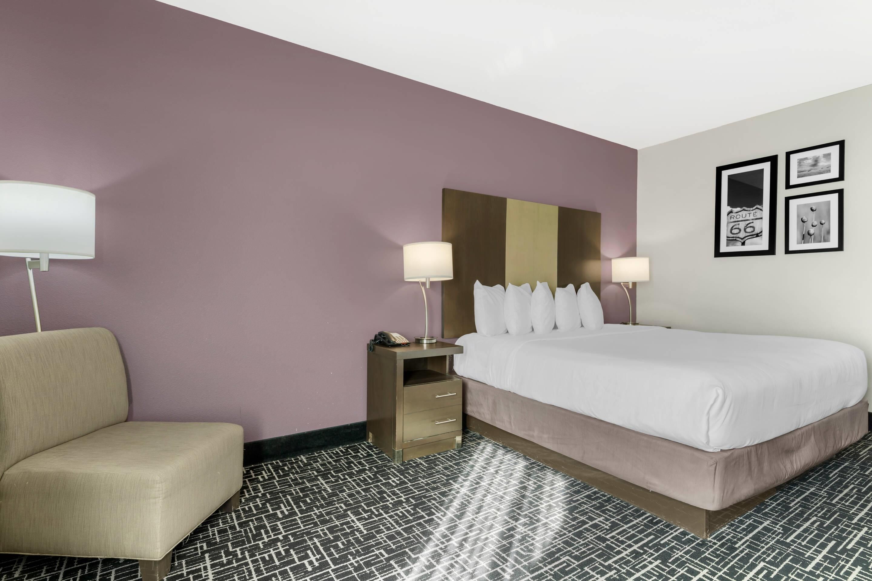 A hotel room with a bed, bedside tables, a chair, and a patterned floor.